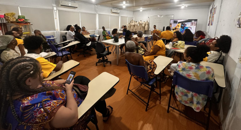 Foto colorida que mostra uma sala de aula do IFRJ, com várias pessoas negras e usando roupas tradicionais afro-brasileiras, coloridas