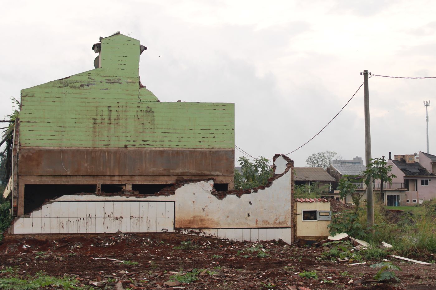 Foto colorida que mostra escombros de casa e, ao fundo, outras residências no bairro Navegantes, em Arroio do Meio