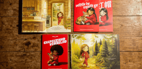Foto com livros das Fábulas Verdes sobre mesa marrom. Na imagem, aparecem quatro livros da Chapeuzinho Vermelho, um aparece a capa, vermelha, com uma menina e um lobo e os outros abertos.