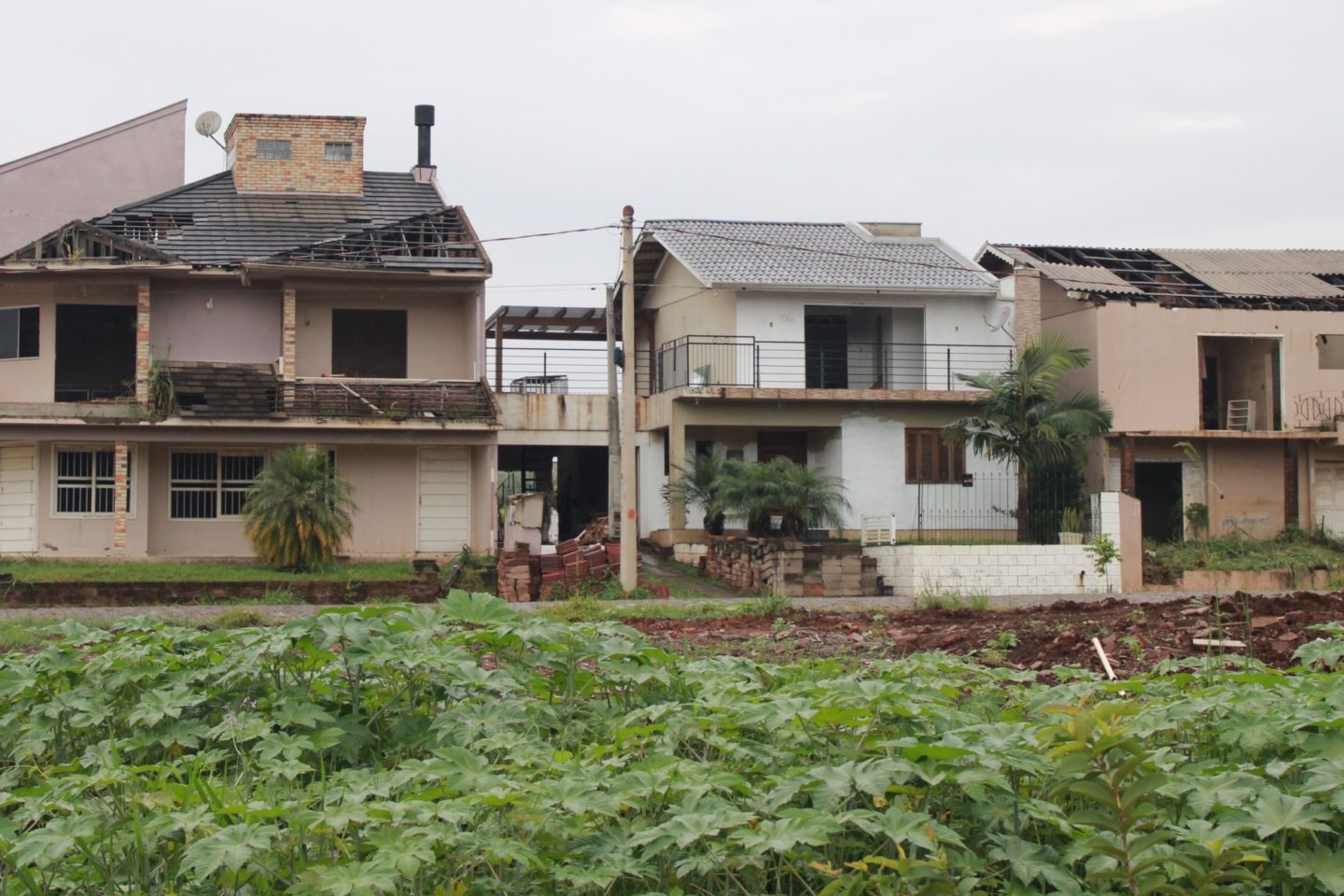Foto colorida que mostra três casas afetadas pelas enchentes no Bairro Navegantes, em Arroio do Meio. As casas apresentam diversas avarias e buracos nos telhados, além de paredes quebradas