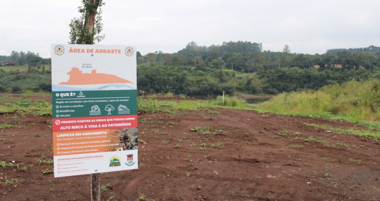 Foto colorida com placa que informa se tratar de uma área de arraste. Ao fundo, terra e margem do Rio Taquari