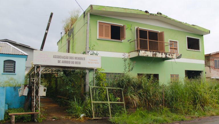 Foto colorida da fachada da antiga sede da Aman, em Arroio do Meio. Na imagem, é possível ver o prédio com portas e janelas abertas e tomado pela vegetação