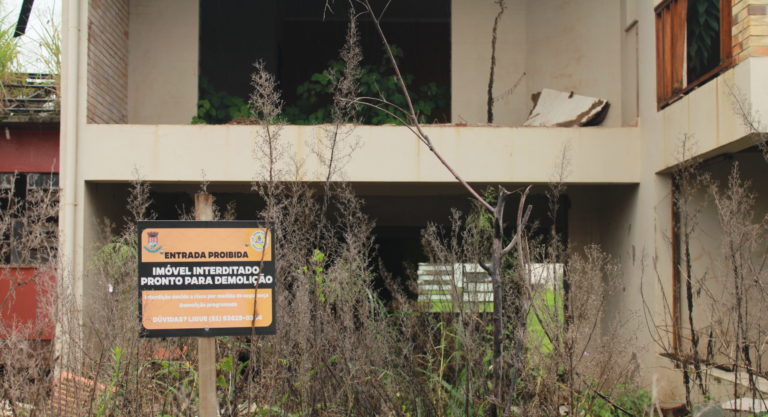 Foto colorida de placa de imóvel interditado em frente à residência destruída pelas enchentes, em Arroio do Meio
