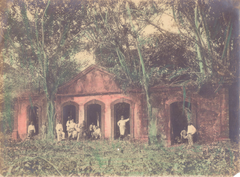 Foto colorida que mostra diversas pessoas em pé diante de construção, rodeada por árvores. Alfredo Clímaco de Carvalho. O Almirante José Carlos de Carvalho, o Dr. Octavio Costa Marques e grupo em visita ao Forte do Príncipe da Beira, 6/07/1913. Costa Marques, Rondônia / Acervo DPHDM