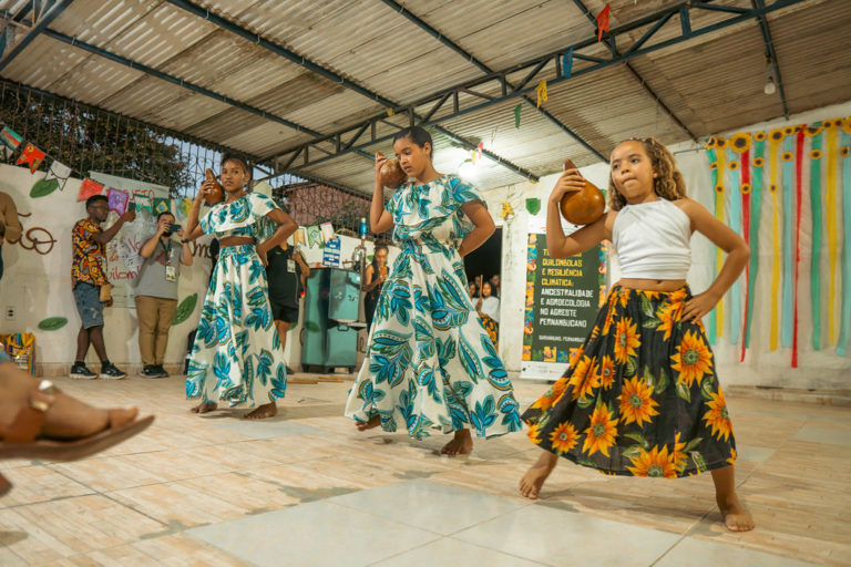 Foto colorida de crianças quilombolas fazendo apresentação de dança tradicional no Espaço Agroecológico Dona Mira, Quilombo Estivas