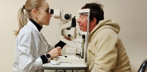 Foto colorida de Quelvin Lima durante consulta com oftalmologista em Porto Alegre. Ele aparece com os olhos em aparelho de visão. Na imagem, uma médica aparece do outro lado do aparelho