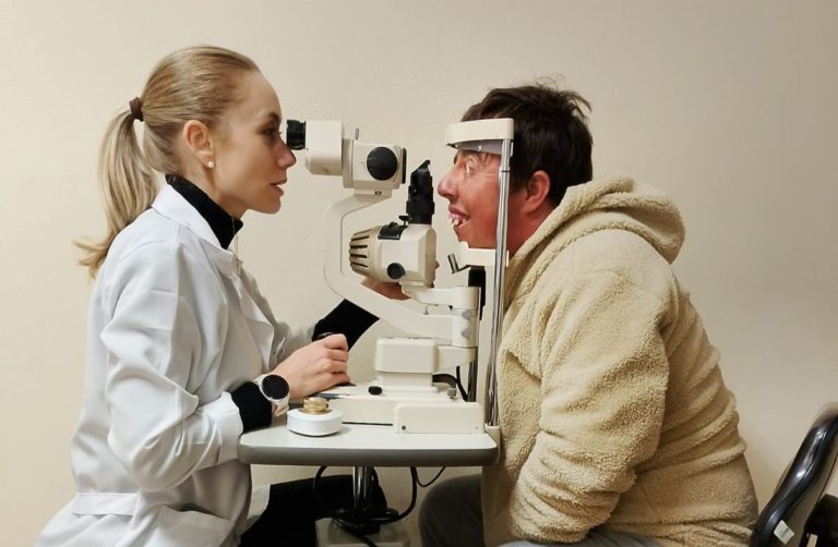 Foto colorida de Quelvin Lima durante consulta com oftalmologista em Porto Alegre. Ele aparece com os olhos em aparelho de visão. Na imagem, uma médica aparece do outro lado do aparelho