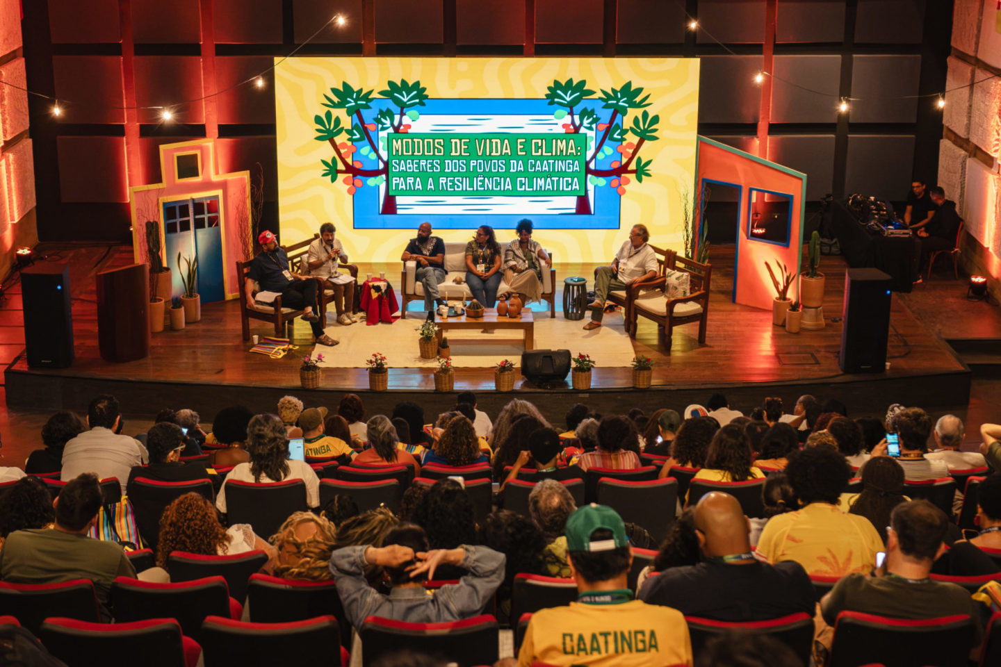 Foto colorida do painel: Modos de vida e clima, que abriu os debates da segunda edição da semana do clima na Caatinga, no Cais do Sertão, em Recife. Na imagem, aparecem os painelistas no centro e o público de costas, assistindo o evento.