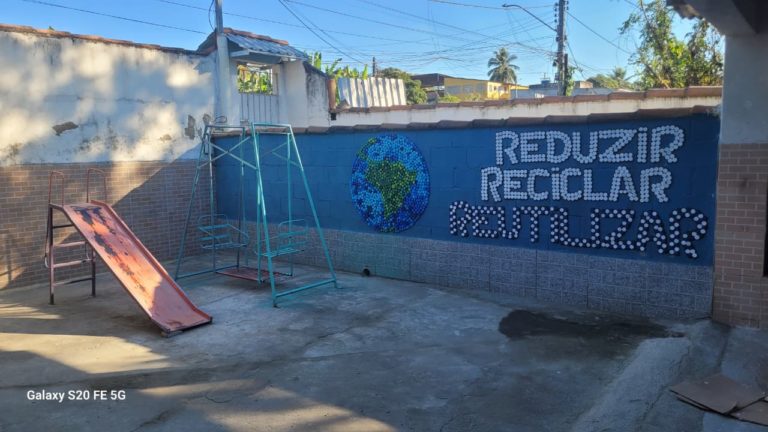 Foto colorida do Pátio da sede da Associação Espaço Gaia, no bairro Fazenda dos Mineiros, um dos sete bairros que constituem o Complexo do Salgueiro. Na imagem, aparece um muro com as palavras reduzir, reciclar e reutilizar.