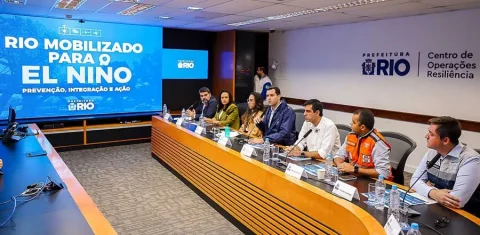 Foto colorida que mostra diversas pessoas reunidas diante de mesa, com um telão ao lado que diz: Rio mobilizado para o El Niño