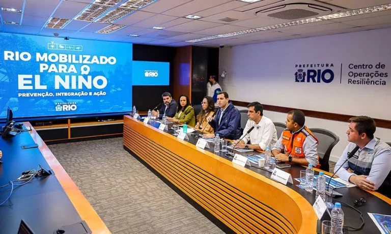 Foto colorida que mostra diversas pessoas reunidas diante de mesa, com um telão ao lado que diz: Rio mobilizado para o El Niño