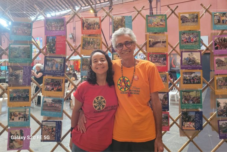 Denise Amador e Rodrigo Junqueira em frente ao mural de fotos da exposição “30 anos Mutirão Agroflorestal”: fortalecimento da consciência socioambiental (Foto: Núbia de Oliveira Iacomini)