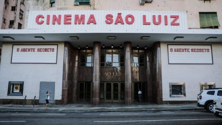 Foto colorida da fachada do Cinema São Luiz, em Recife. Na imagem, é possível ver a porta de entrada do espaço e, ao lado, anúncio em letras vermelhas do filme O Agente Secreto