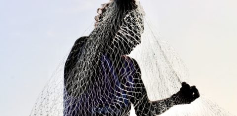 Foto colorida que mostra silhueta de pescador na ilha de Jubim. Na imagem, a pessoa está segurando uma rede de pesca