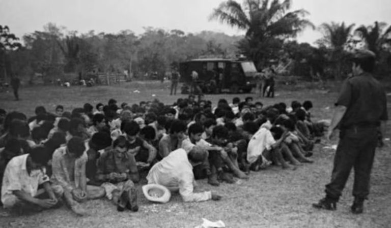 Posseiros rendidos reunidos no acampamento sob vigilância de um policial militar (Foto: 'Corumbiara, caso enterrado', Editora Elefante / Reprodução)