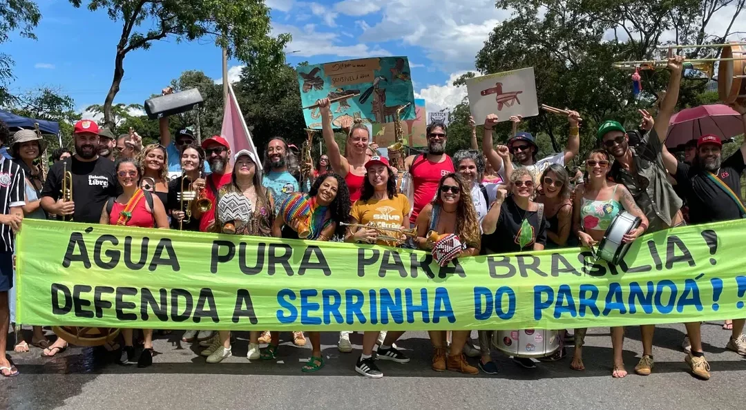 Foto colorida com pessoas em manifestação em defesa da Serrinha do Paranoá. Na imagem, as pessoas aparecem em pé e segurando uma faixa que diz: água pura para Brasília! Defenda a Serrinha do Paranoá